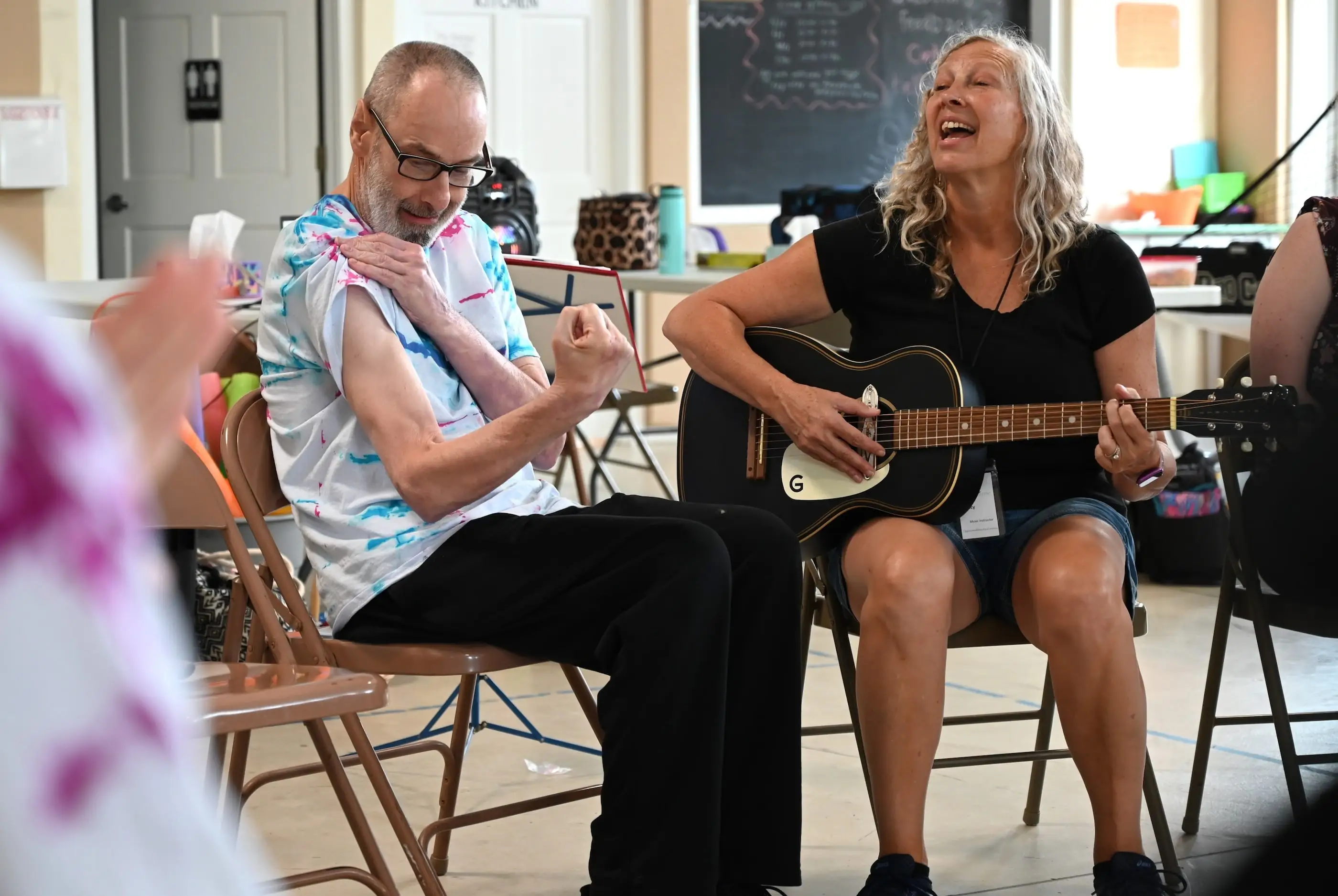 Man flexing is muscle as woman sings. They are having fun together in group sing along.